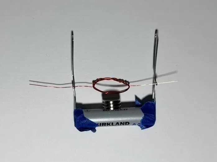 A copper wire coil balanced on two paperclips above a magnet on a AAA battery