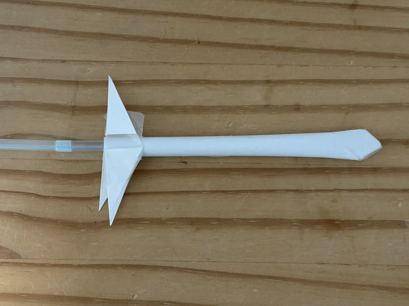 A paper straw rocket with four card fins, resting on its launch straw
